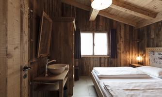 A cozy bedroom with wooden walls and a double bed. The room features a sink and a window that lets in natural light.