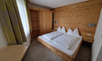 A cozy bedroom with a double bed and wooden furniture. The room has large windows that let in plenty of daylight.