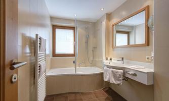 A modern bathroom with a bathtub and a shower. The room features large windows and a practical washbasin.