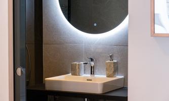 A modern bathroom with an elegant sink and a lighted mirror. The decor is simple and stylish, featuring a minimalist design.