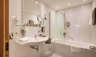 A modern bathroom with a bathtub and shower. It features bright tiles and a large mirror surface.
