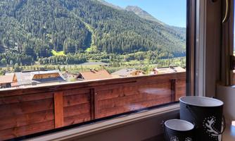 View from a window of a green mountain landscape with forests and hills. In the foreground, two cups are on the windowsill.
