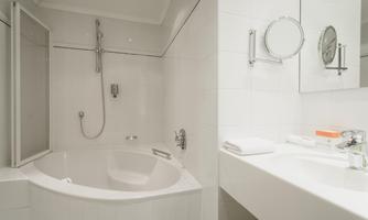 A modern bathroom with a bathtub and a shower. The walls are bright and the furnishings are simple and clean.