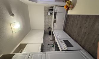 A modern kitchen with white cabinets and gray tiles. On the countertop, there is a bowl of fresh fruits.