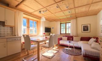 A cozy living space with a modern kitchen, a dining table, and a bright seating area. Large windows provide plenty of daylight.