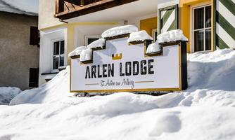 A sign of the Arlen Lodge in a snowy environment. The snow lies around the building and the sun is shining.