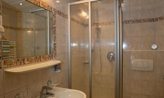 A modern bathroom with a shower, sink, and toilet. It is bright and clean, with modern tiles and a large mirror.