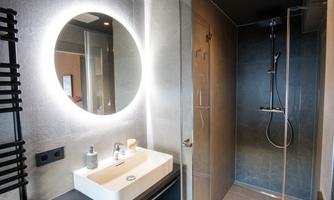 A modern bathroom with a large, illuminated round mirror. The shower area is elegant and well-designed.