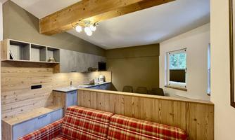 A cozy living area with a checked sofa and an open kitchenette. Wooden paneling and a bright environment create an inviting atmosphere.