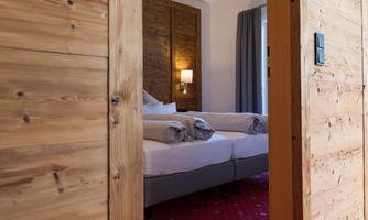 A cozy hotel room with two beds, surrounded by warm wood. Light streams through the window, creating an inviting atmosphere.