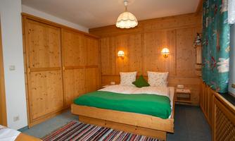 A cozy bedroom with wooden furniture and a double bed. The walls are paneled with wood, and colorful curtains add a splash of color to the room.