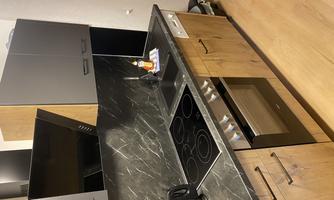 A modern kitchen with wood and dark accents. The room features a stove, a sink, and a kettle.