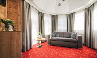 A cozy living area with a gray sofa and red carpet. Large windows let in plenty of daylight and create a friendly atmosphere.