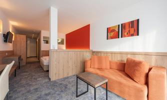 A modern room with an orange sofa and a small table. The walls are partially paneled with wood, and there are colorful artworks.