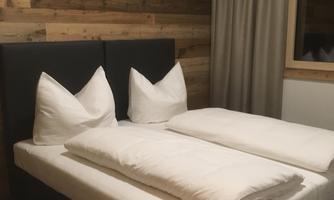 A comfortable bedroom with a large double bed and modern, bright pillows. The walls are made of wood, creating a cozy atmosphere.