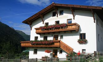 A charming, multi-story house with balconies and flower boxes. In the background, mountains and a blue sky are visible.