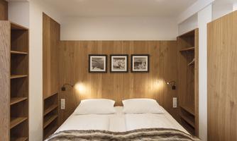 A cozy bedroom with a double bed and wooden shelves. Three pictures hang on the wall and the lighting is soft.