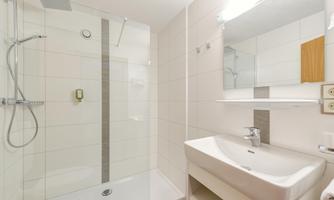 A modern bathroom with a walk-in shower and a sink. The walls are brightly tiled, and a large mirror creates a pleasant atmosphere.