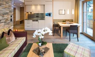 A modern living room with an open kitchen. Cozy furniture and a decorative orchid on the table create an inviting atmosphere.