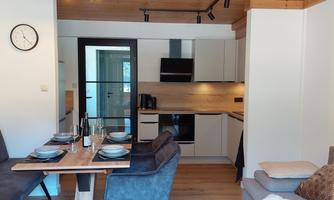 A modern apartment with an open kitchen and dining area. The space is bright and inviting, with wooden ceilings and stylish furnishings.