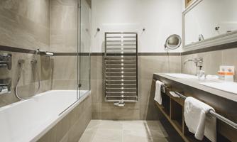 A modern bathroom with a bathtub and a separate shower. The space is elegantly designed, featuring a wooden shelf and towels.