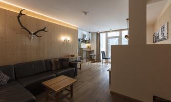 A cozy living room with wooden paneling and modern furnishings. The room offers plenty of natural light through large windows.