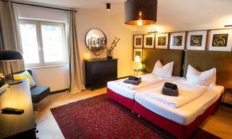 A modern bedroom with two beds and elegant furnishings. The walls are adorned with artworks, and a cozy armchair is placed in the corner.