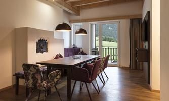 A modern dining room with a large table and colorful chairs. Large windows provide a view of the landscape.