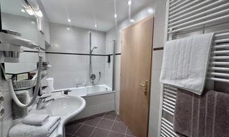 A modern bathroom with a bathtub and shower facility. The walls are brightly tiled, and towels are hanging on a radiator.