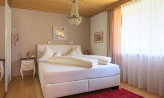 A cozy bedroom with a large white bed and a red carpet. The walls are light, and a chandelier provides pleasant light.