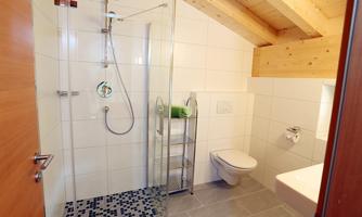 A modern bathroom with a glass shower and a clear, minimalist design. The walls are bright tiled, and the wooden ceiling creates a warm atmosphere.