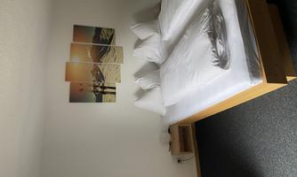 A simple bedroom with two beds and modern white bed covers. On the wall hangs a multi-part picture of a mountain landscape and sunset.