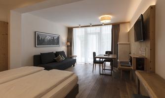 A modern room with two beds, a sofa, and a table. Large windows provide plenty of natural light.