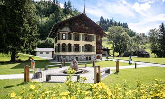 A beautiful building in traditional style, surrounded by trees and meadows. Flowers are blooming in the foreground and the landscape is well-maintained.