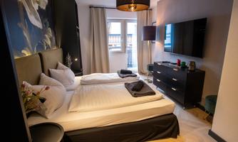 A modern room with two single beds and a television. The walls are in neutral colors and there are windows with curtains.