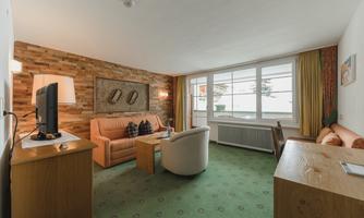 A cozy living room with wood paneling and large windows. There is a sofa, a television, and a table.