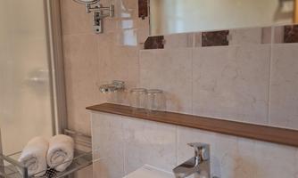 A modern bathroom with an elegant sink and a large mirror. Towels are neatly arranged, and the walls are tiled in neutral tones.