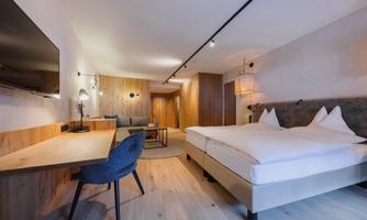 A modern room with a large double bed and a stylish desk. The wooden elements and soft lighting create a warm atmosphere.