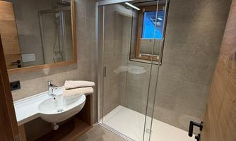 A modern bathroom with a glass shower cubicle and a sink. The room is bright and stylishly furnished.