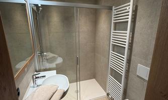 A modern bathroom with a glass shower and a toilet. The walls are in neutral tones, and there is a towel heater.