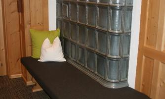 A modern wooden bench with a gray cushion. In the background, there is a decorative wall made of old metal panels.
