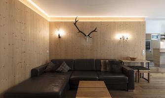 A modern living room with wood paneling and a large, dark brown sofa. Antlers and stylish wall lamps hang on the wall.