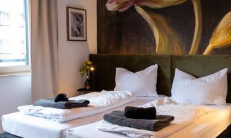 A cozy bedroom with two beds and elegant decoration. A large flower painting hangs on the wall, and the light gently streams through the window.