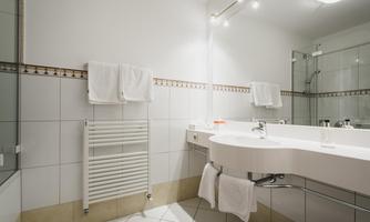 A modern bathroom with a white tiled wall and an elegant shower. Fresh towels are neatly hung.