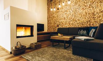 A cozy living room with a fireplace and a wooden ceiling. The room is modernly furnished and invites relaxation.
