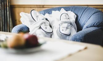 A cozy armchair with a white bathrobe and slippers. In the foreground, there is a bowl of fresh fruit.