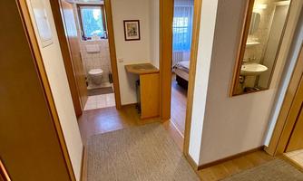 A bright hallway with wooden floors and carpets. There are several doors to the adjoining rooms and a small table.