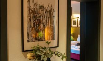 An elegant hallway with a modern artwork on the wall. In the background, a cozy room with a bed is visible.