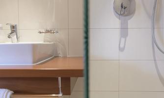 A modern bathroom with a sink and a shower area. The walls are tiled, and the floor has an appealing pattern.