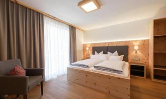 A modern bedroom with a large double bed and light wooden furniture. Large windows provide plenty of daylight and a cozy atmosphere.